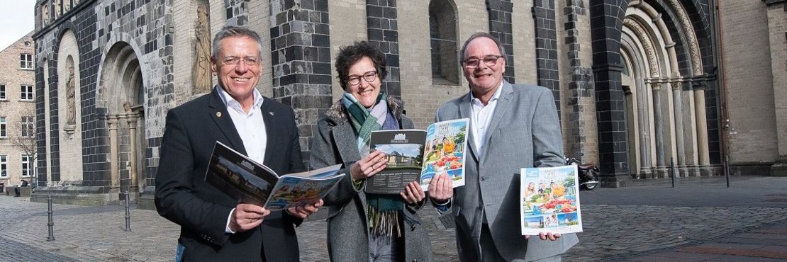 Landrat Hans-Jürgen Petrauschke, Tourismusförderin Steffi Lorbeer und Robert Abts stehen auf einem Platz und halten den Kultur- und Freizeitführer in der Hand