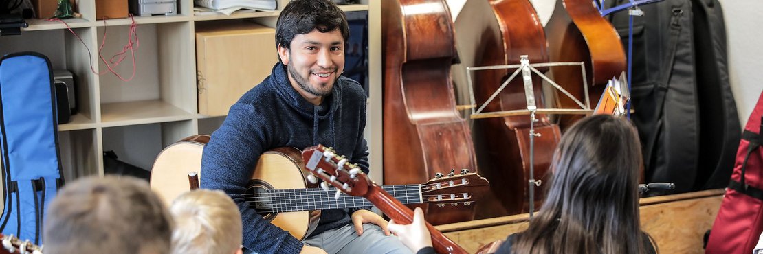 Männliche Person mit Gitarre vor einer Gruppe Kindern