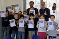 Zwei erwachsene männliche Personen mit einer Gruppe Kindern, die Urkunden hochhalten