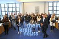 Landrat Hans-JürgenPetrauschke steht mit einer großen Gruppe junger Frauen und Männer im großen Kreissitzungssaal Grevenbroich. Die jungen Menschen halten Laptops in Ihren Händen. 