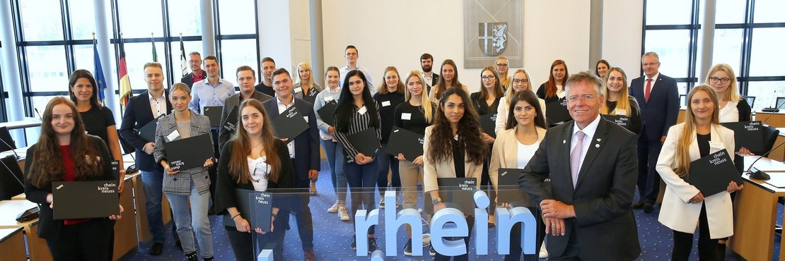 Landrat Hans-JürgenPetrauschke steht mit einer großen Gruppe junger Frauen und Männer im großen Kreissitzungssaal Grevenbroich. Die jungen Menschen halten Laptops in Ihren Händen. 