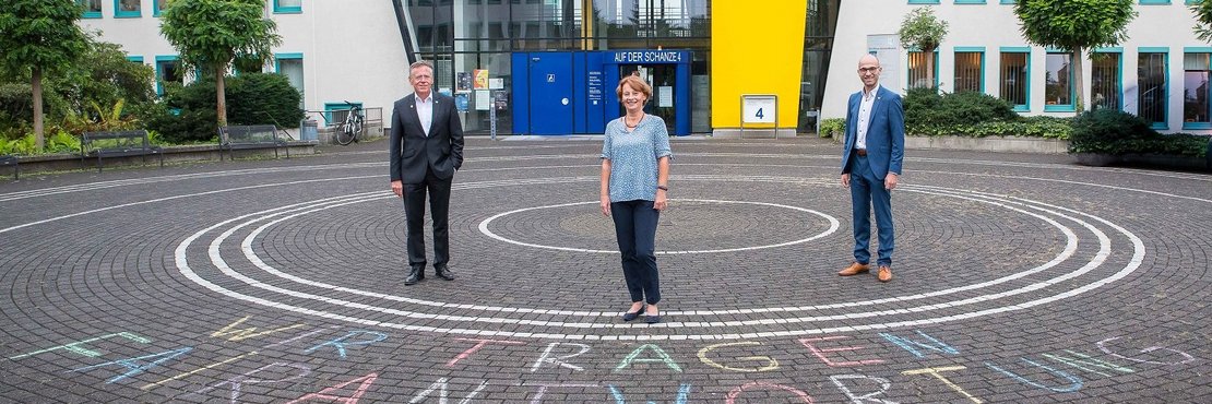 Landrat Hans-Jürgen Petrauschke, Benjamin Josephs und Renate Kuglin stehen vor dem Kreishaus in Grevenbroich. Auf dem Boden vor Ihnen steht mit Kreide "Wir tragen Fairantwortung" geschrieben. 