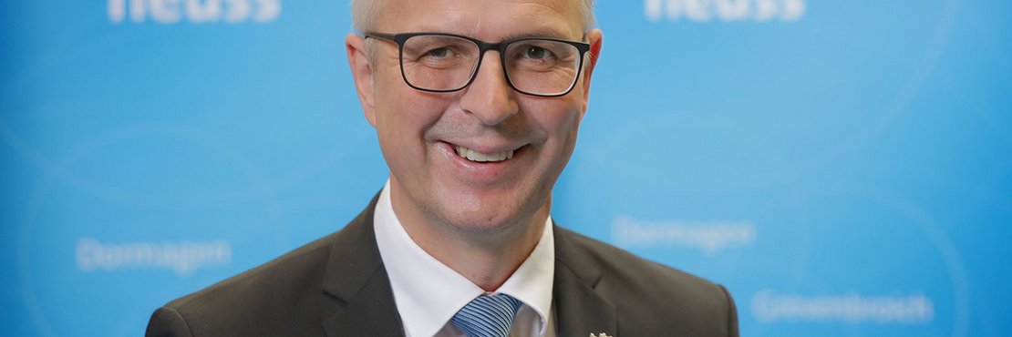 Kreisdirektor Dirk Brügge vor blauer Wand mit Logo Rhein-Kreis Neuss