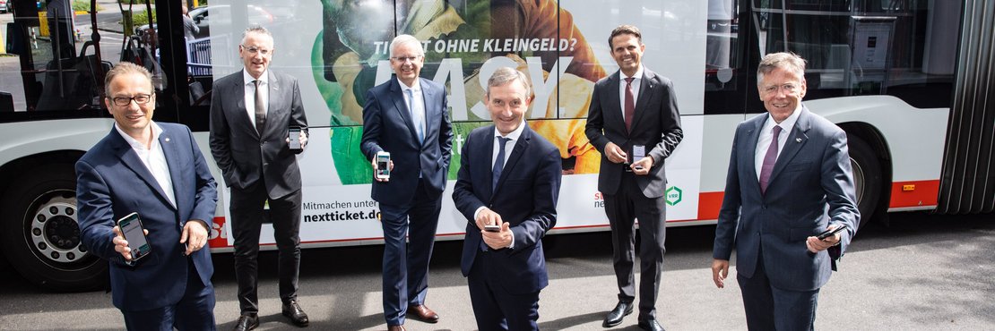 Die 6 Herren stehen vor einem Linienbus und halten Ihre Smartphones in den Händen