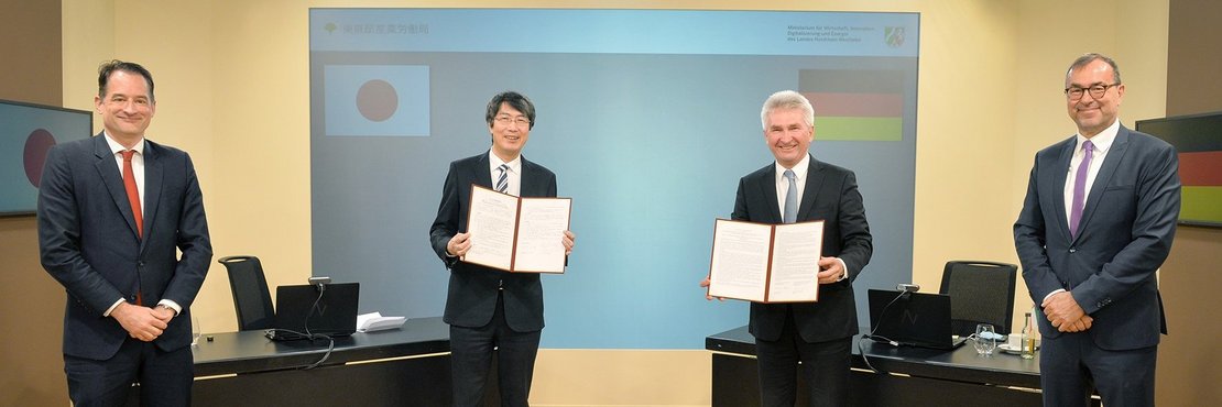 Felix Neugart, Kiminori Iwama, Minister Andreas Pinkwart und Karl-Uwe Bütof in Besprechungsraum. Man steht die deutsche und die japanische Flagge auf einer Leinwand im Hintergrund.