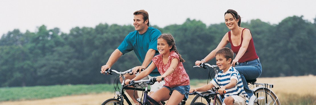 Eine 4-köpfige Familie mit Fahrrädern auf einem Feldweg