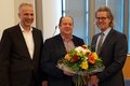 Drei Personen - die mittlere Person hält einen Blumenstrauß