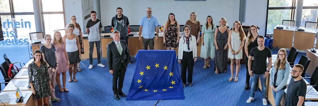 17 junge Menschen stehen im Halbkreis im Kreissitzungssaal in Grevenbroich. In der Mitte davor: Landrat Hans-Jürgen Petrauschke und Ruth Harte neben einer großen  Europafahne