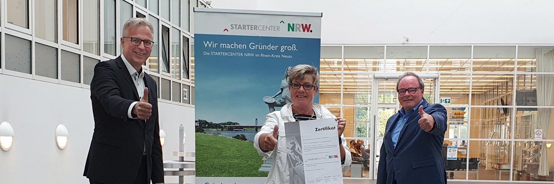 Dirk Brügge, Hildegard Fuhrmann und Robert Abts stehen vor einem Plaket mit der Aufschrift "Statercenter NRW"