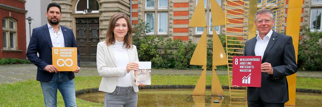 Thiago de Carvalho Zakrzewski mit Schild: "12 Nachhaltige/r Konsum und Produktion"; Verena Tranzer mit Broschüre und Hans-Jürgen Petrauschke mit Schild "8 Menschenwürdige Arbeit und Wirtschaftswachstum"