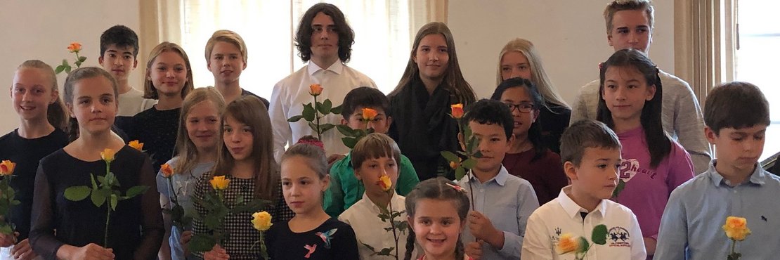 Personengruppe überwiegend Kinder mit gelben Rosen in den Händen
