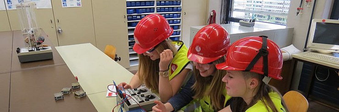 Drei Schülerinnen mit Schutzkleidung arbeiten mit einem elektronischen Gerät.