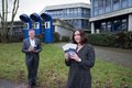 Landrat Hans-Jürgen Petrauschke und Melanie Erdmann stehen auf der Wiese vor dem Gebäude des Berufskollegs BTI und halten die Brpschüren in dern Händen.