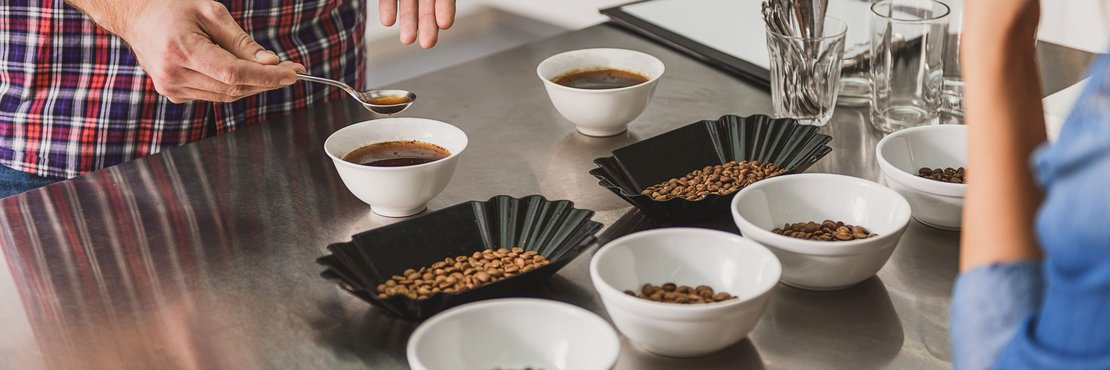 Eine Person zeigt einer anderen verschiedene Kaffeesorten, die in Schalen gefüllt sind