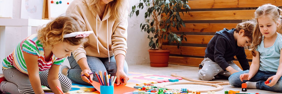 dekorativ, Betreuungsperson mit spielenden Kindern auf dem Boden sitzend