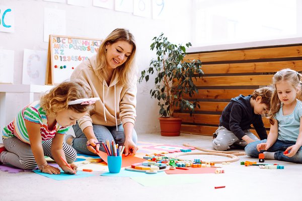 dekorativ, Betreuungsperson mit spielenden Kindern auf dem Boden sitzend