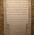 Weiß-silbriger Wandbehang, der in geometrische Felder unterteilt ist vor einer Backsteinwand. © KreisMuseum Zons