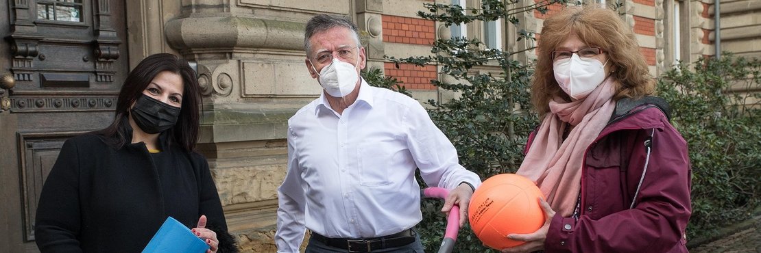 Die in der Bildbeschreibung genannten Personen stehen mit Sportgeräten vor dem Grevenbroicher Ständehaus. Sie tragen Mund-Nasenschutz. 