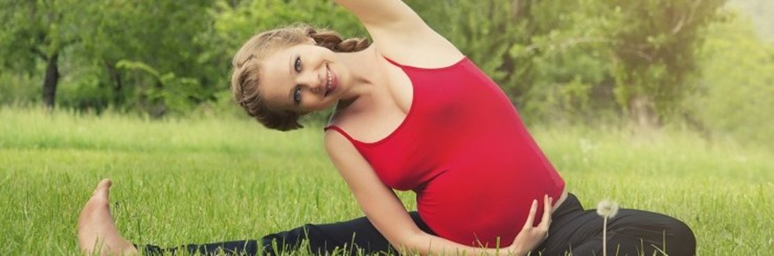 Schwangere Frau macht Gymnastikübungen auf einer Wiese