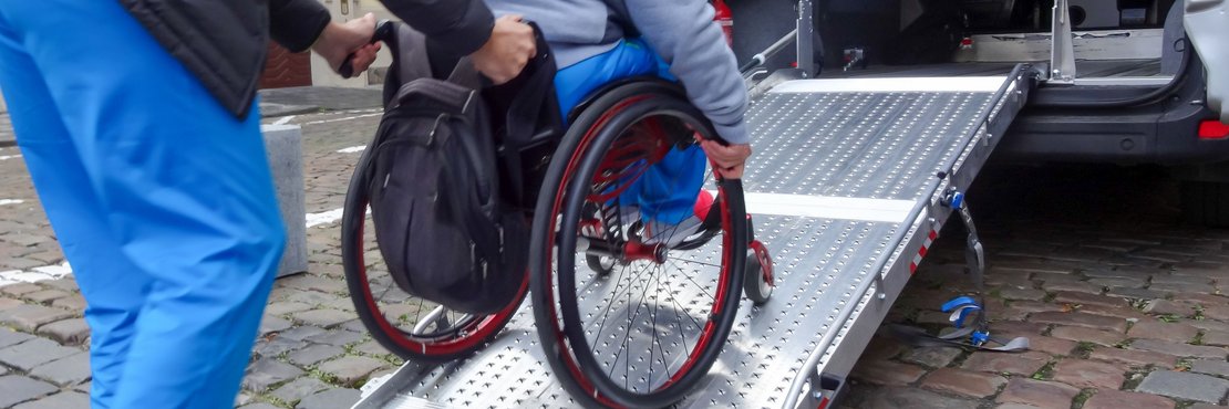 Ein Rollstuhlfahrer wird über eine Rampe in ein Fahrzeug geschoben.