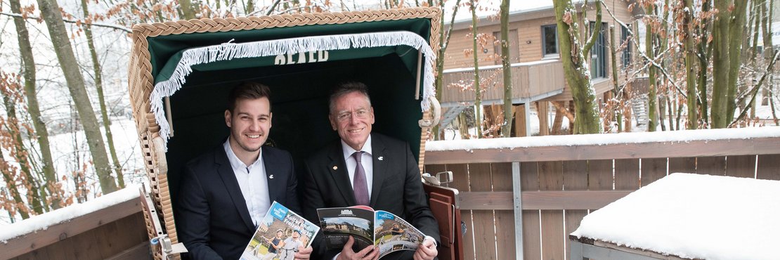 Landrat Hans-Jürgen Petrauschke und Tourismusbeauftragter Michael Ruß präsentieren den Kultur- und Freizeitführer auf dem Balkon eines Baum-Chalets im Alpenpark Neuss.