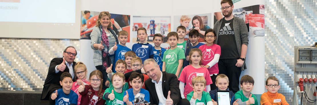 Gruppenfoto mit den Teams der Gillbachschule Rommerskirchen: Strahlende Gesichter bei den „BRG bluerobogillbachs“, die Glückwünsche von Kreisdirektor Dirk Brügge (M.) und Roberts Abts (l.), Geschäftsführer der Wirtschaftsförderungsgesellschaft Rhein-Kreis Neuss, entgegen nahmen.