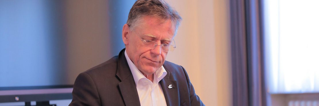 Landrat Hans-Jürgen Petrauschke sitzt am Schreibtisch, blickt ernst auf seine Unterlagen