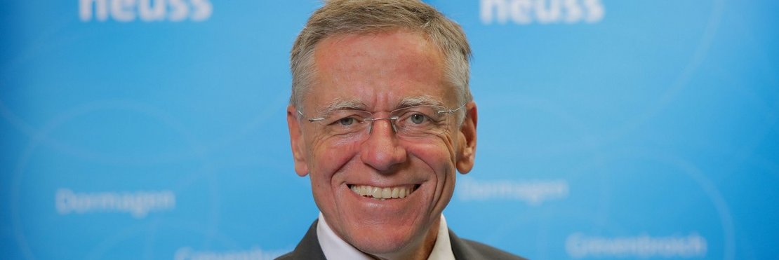 Landrat Hans-Jürgen Petrauschke lächelnd vor einer hellblauen Wand