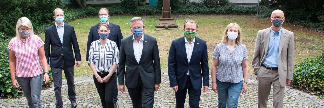 Landrat Hans-Jürgen Petrauschke steht mit Ursula Heinrichs, Thomas Dückers, Gregor Küpper, Natalia Jefimenko, Dr. Martin Mertens, Ulrike Schmitz-Doering und Harald Zillikens vor dem Kreisjugendamt. Alle tragen einen Mund-Nasenschutz. 