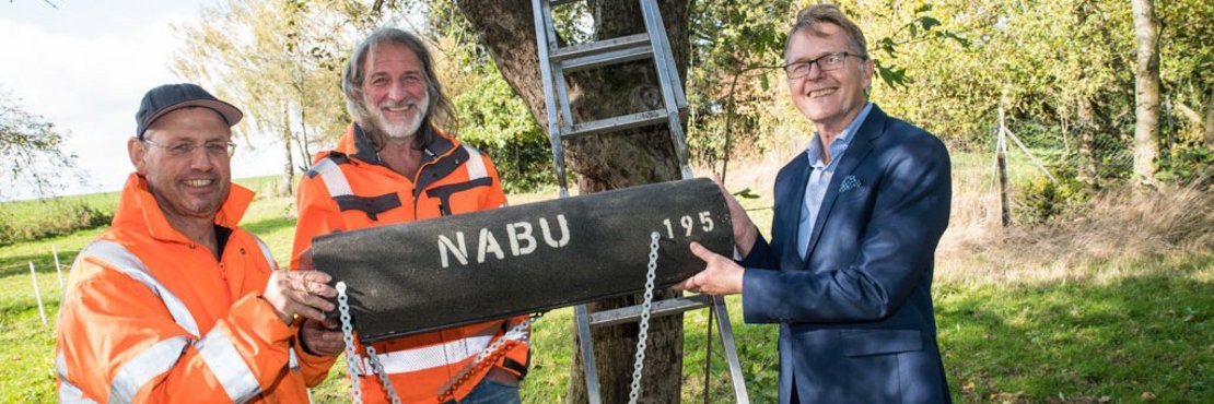 Die drei Männer halten künstliche Nisthöhle; stehend vor Baum