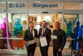  Landrat Hans-Jürgen Petrauschke, Bürgermeister Erik Lierenfeld und der Leiter des Bürgeramtes Michael Feiser stehen mit Fahrzeugpapieren und Nummernschild vor dem Bürgeramt.