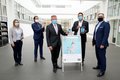 Landrat Hans-Jürgen Petrauschke steht mit einer Frau und frei Herren im Lichthof des Kreishauses Neuss. Landrat Petrauschke und Digitalisierungsmanager Brings halten ein Smartphone bzw. ein Tablet auf dem die Navigatoions-App zu sehen ist.  Mittig auf dem Boden steht ein Plakat mit der Überschrift "Kennen Sie unsere Gebäude-Navigation?" und Hinweisen zur App.