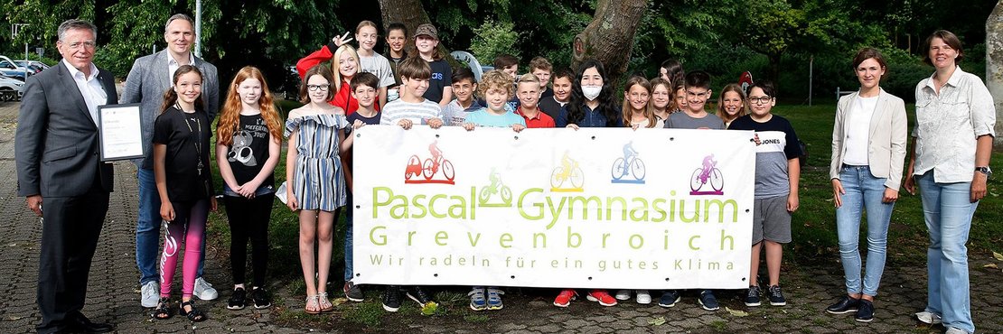 Siehe Bildbeschreibung. Die Schüler'innen halten ein Banner mit der Aufschrift: Pascal Gymnasium Grevenbroich. Wir radeln für ein gutes Klima  