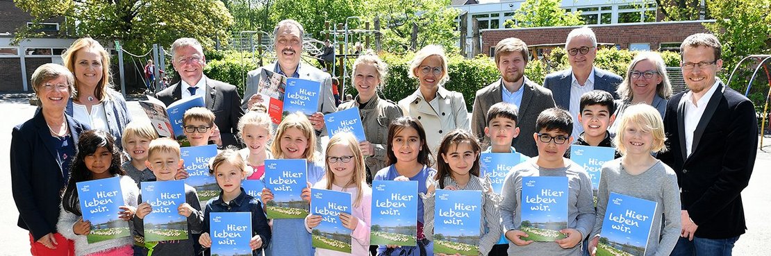 Präsidentin Beate Pricking (links), Landrat Hans-Jürgen Petrauschke (hinten links), und Stephan Meiser (hinten 2.v.l.) von der Sparkasse Neuss mit einer Gruppe von Kindern, die ein Heft in den Händen halten.