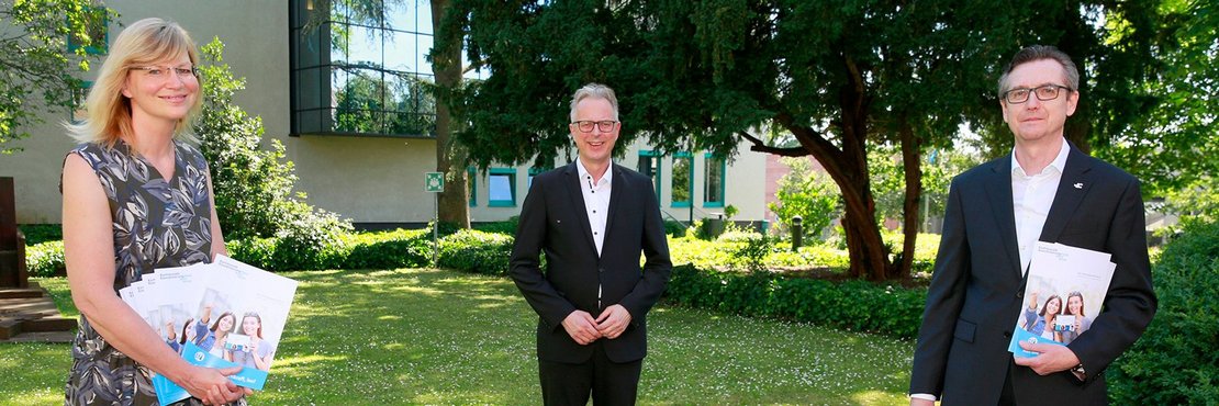 Die genannten Personen stehen auf einer grünen Wiese. 2 halten Broschüren in der Hand.