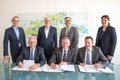 Personen stehen und sitzen in zwei Reihen an einem Tisch: Ernst Thüner, Dirk Hunke, Harald Vieten und Ines Manolias, unten von links Stephan Lommetz, Landrat Hans-Jürgen Petrauschke und Dirk Reimann