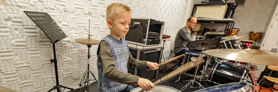 Junge am Schlagzeug. Im Hintergrund der Schlagzeuglehrer der Musikschule Rhein-Kreis Neuss