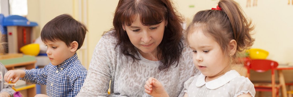 Eine Frau spielt mit zwei Kleinkindern an einem Tisch