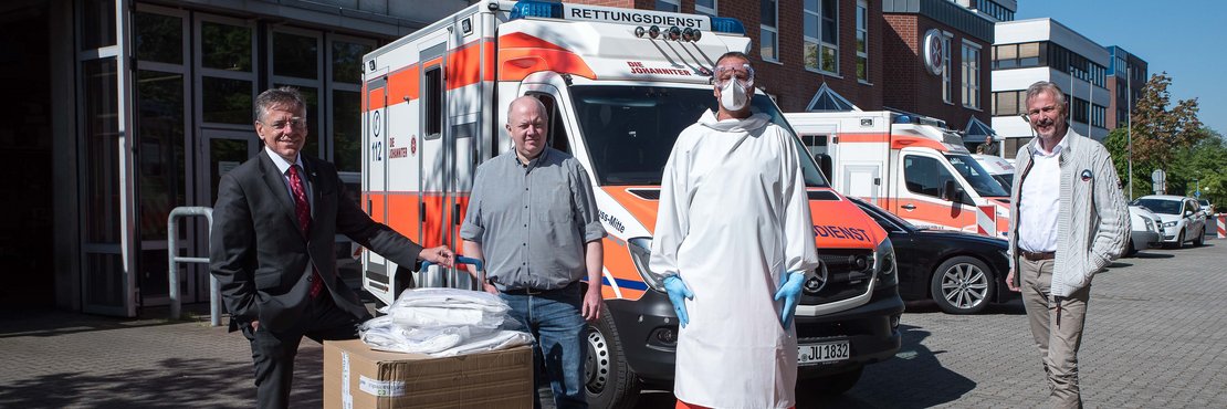 Landrat Hans-Jürgen Petrauschke und Kreisdirektor Dirk Brügge mit dem Leiter der Rettungswache Neuss Mitte Heiko Kraus und Thorsten Holz mit Kartons vor einem Rettungswagen