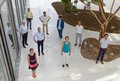Eine Gruppe von menschen steht mit Abständen zueinander in Dreiecksform im Innenhof eines hellen Gebäudes. Das Foto ist schräg von oben forografiert.
