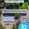 Das Bild zeigt eine Luftaufnahme der Herbert-Karrenberg-Schule. Man sieht das Schulgebäude mit umliegendem Gelände, inklusive Spielplatz. Im unteren rechten Bildbereich ist ein Logo mit der Aufschrift „50 Jahre | 50 Orte“ und „rhein kreis neuss“ zu sehen, was auf ein Jubiläum hindeutet.  Das Bild wirkt sachlich und informativ. © Rhein-Kreis Neuss