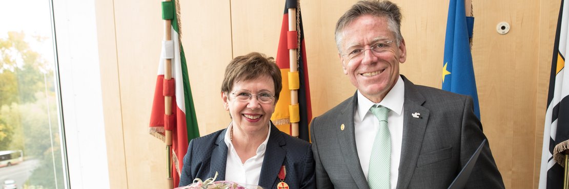 Eine männliche und eine weibliche Person mit Blumenstrauß und Urkunde