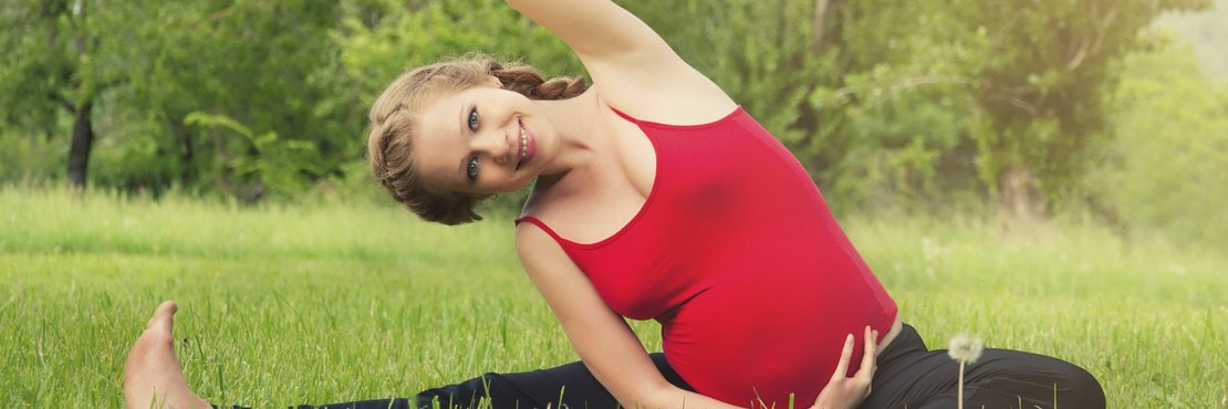 Schwangere Frau macht auf einer Wiese Gymnastikübungen.