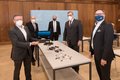 Die in der Bildbeschreibung genannten Herren stehen mit Mund-Nasenschutz und Abstand um einen Tisch mit technischen Geräten
