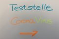 Blatt mit buntem Schriftzug Teststelle Corona Virus und Pfeil nach rechts