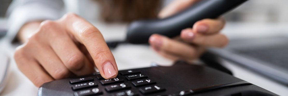 Ein Mensch hat einen Telefonhörer in der Hand und tippt auf das Bedienfeld