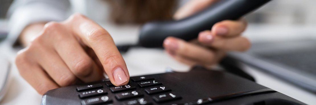 Ein Mensch hat einen Telefonhörer in der Hand und tippt auf das Bedienfeld