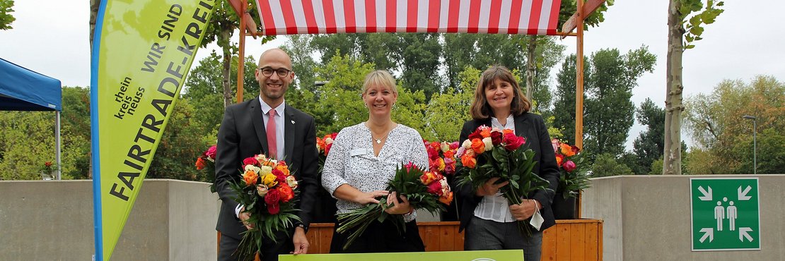 Kreis-Pressesprecher Benjamin Josephs, Melanie Schröder und Petra Koch vor einem Stand mit fairen Rosen