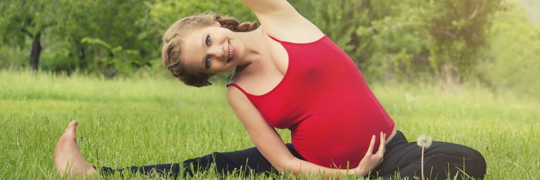 Schwangere Frau macht Gymnastik auf einer Wiese