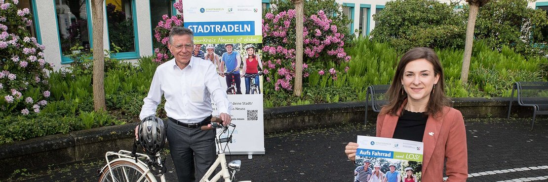 Hans-Jürgen Petrauschke mit Fahrrad und Verena Tranzer mit Plakat werben für die Aktoin Stadtradeln.